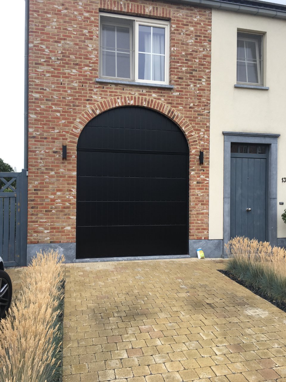 Zwarte sectionale garagepoort met rondboog in een bakstenen gevel, hersteld door M-Vision