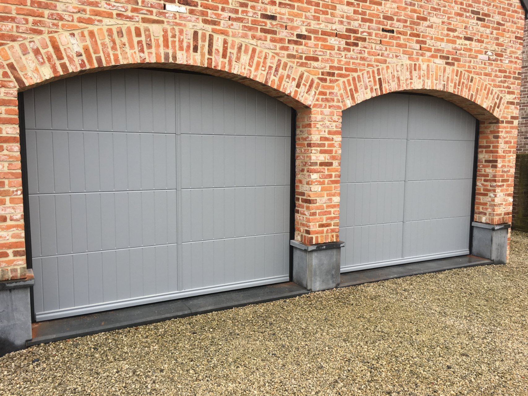 Twee grijze sectionale garagepoorten met rondboog aan een woning, onderhoud en herstelling door M-Vision
